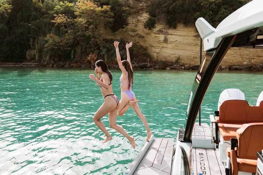 Two people jumping off a boat into turquoise water surrounded by cliffs. 5