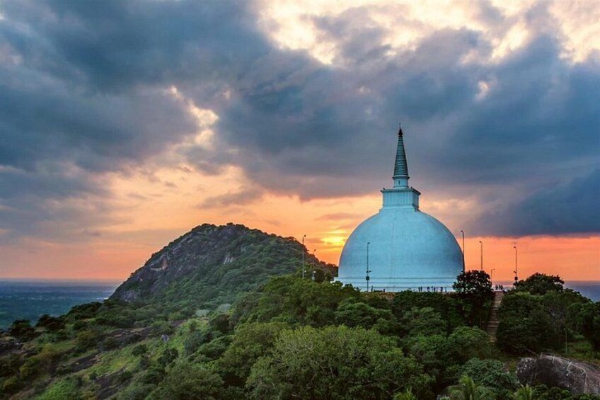 A white dome-shaped structure with a spire, surrounded by lush greenery and hills, under a cloudy sky. 5