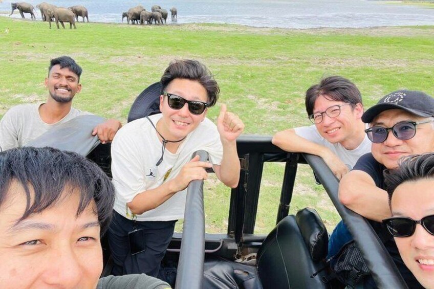 A group of people on a safari vehicle near a water body with elephants in the background. 3