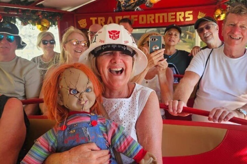 A group of people on a red vehicle with a 'Transformers' sign, a doll, and a person wearing a white hat. 1