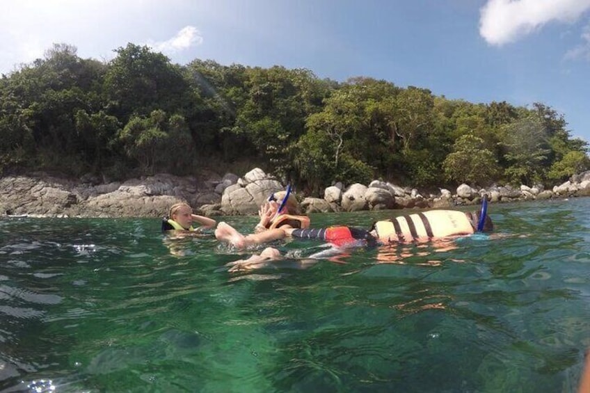 Människor som snorklar i klart vatten med en stenig kustlinje och träd i bakgrunden. 5