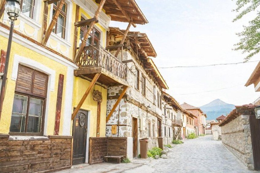 Una calle adoquinada flanqueada por edificios tradicionales, balcones de madera y una montaña al fondo. 3