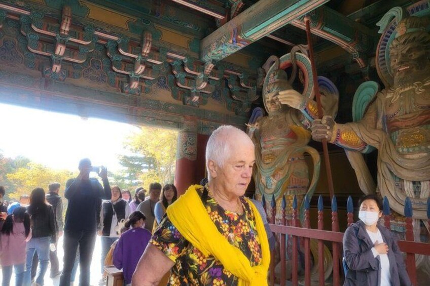 A person in a yellow floral dress standing in front of a traditional Asian architectural structure with intricate carvings and a large, ornate statue. 4