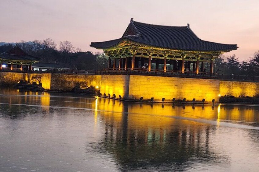 A traditional Korean building with a tiled roof, illuminated by warm lights, reflecting on a calm body of water. 2