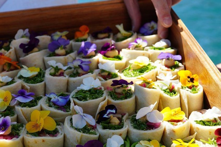 Een houten dienblad met gerolde hapjes, versierd met kleurrijke bloemen. 2
