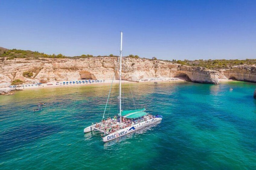 Een zeilboot genaamd 'DISCOVERER' op turquoise water, met rotsachtige kliffen op de achtergrond. 1