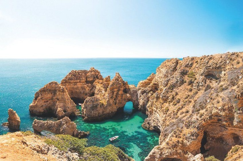 A coastal landscape with rocky formations, a clear blue sea, and a small boat. 5