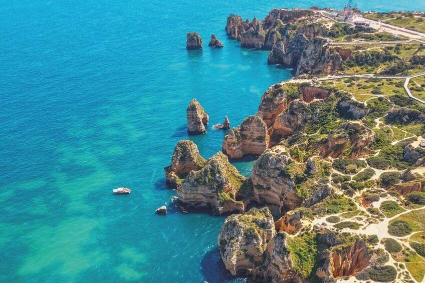 A coastal landscape with rocky formations, clear blue water, and a winding road. 4