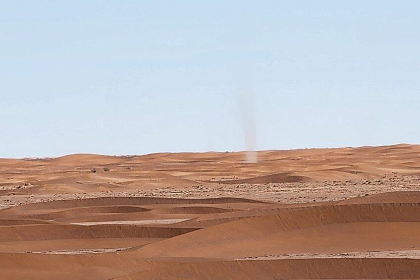 A desert landscape with undulating sand dunes and a distant plume of smoke. 4