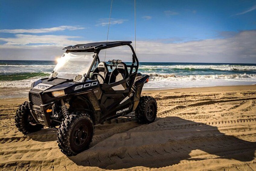 A Polaris 900 ATV parked on a sandy beach with the ocean in the background. 1