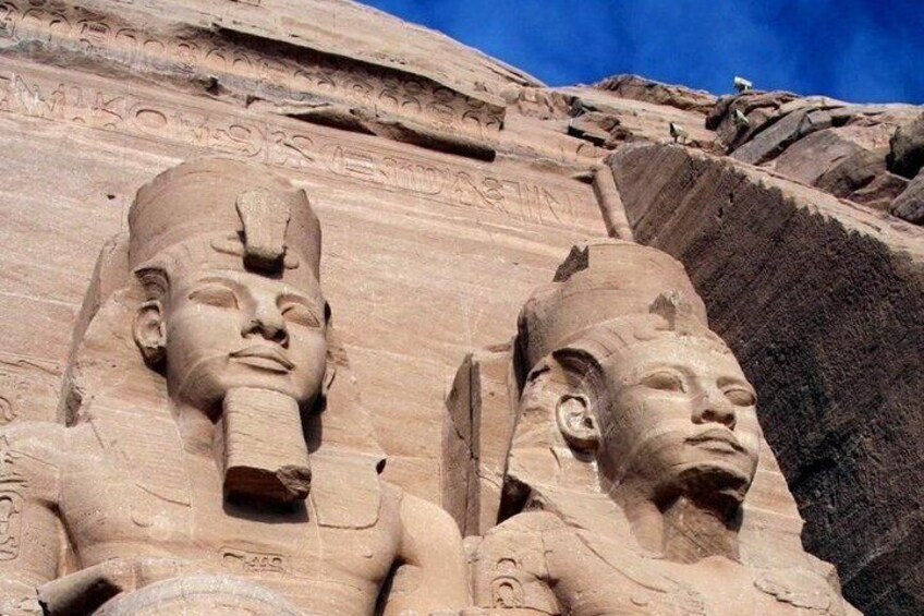 Two large stone statues of pharaohs with hieroglyphics on the wall behind them. 2