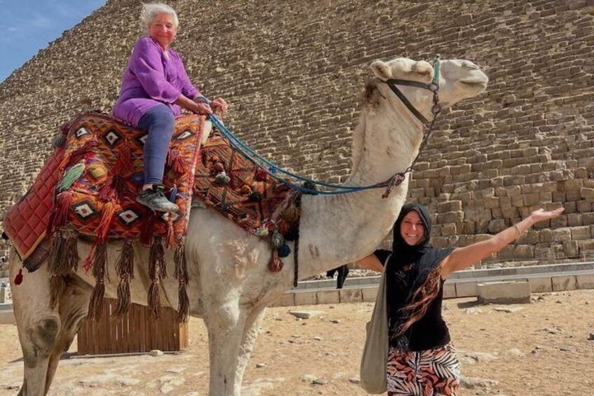 A person riding a camel with a colorful saddle in front of a large pyramid. 3