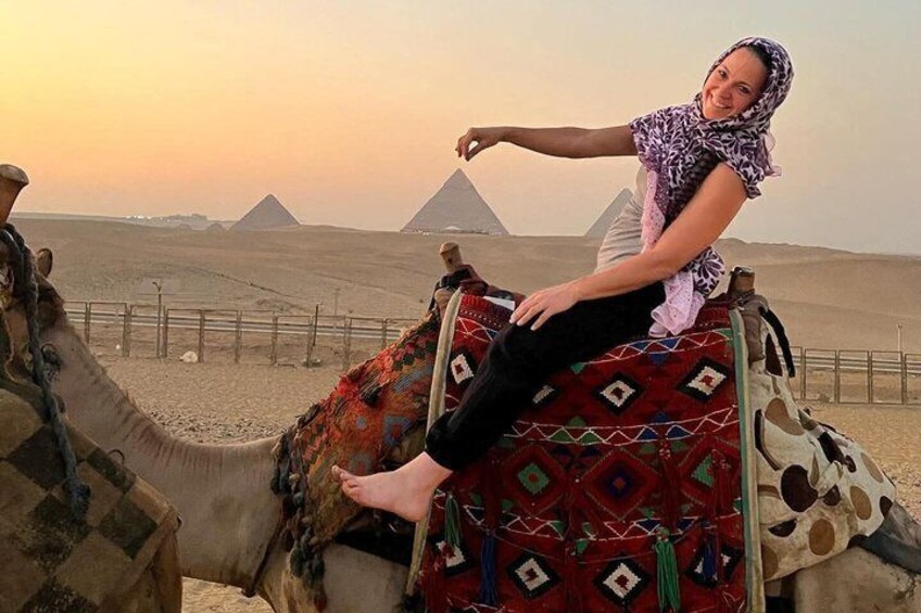A person riding a camel in a desert with pyramids in the background. 1