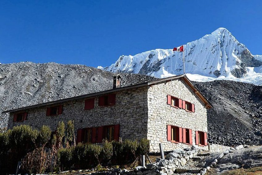 A stone building with red shutters, a flag, and a snow-capped mountain in the background. 1