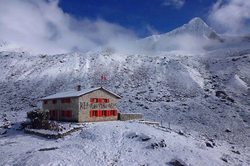 A snow-covered mountain with a small building with red shutters and a flag on top. 2