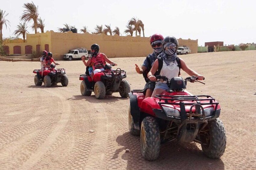 Tres personas paseando en cuatrimotos rojas por un sendero arenoso, con palmeras y un edificio al fondo. 3