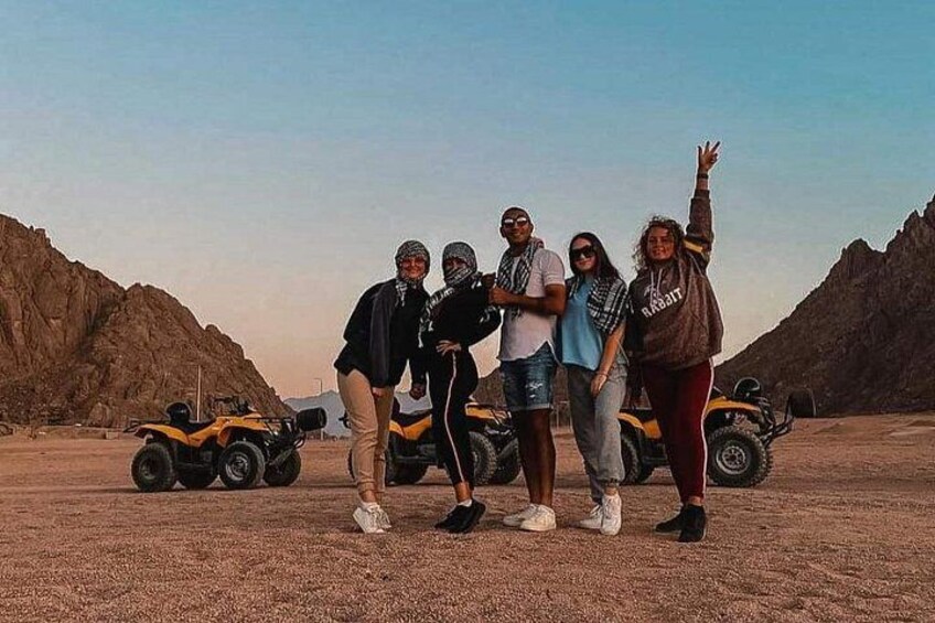 Un grupo de personas posando con vehículos todo terreno en un paisaje desértico con terreno rocoso y montañas al fondo. 2