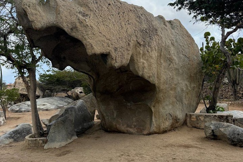 Una gran formación rocosa con una abertura parecida a una cueva, rodeada de rocas más pequeñas y árboles. 1