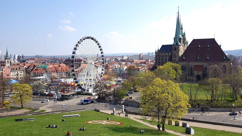 A cityscape with a large Ferris wheel, a church with a tall spire, and a park with people. 4