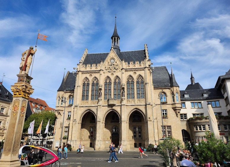 A historic building with a clock tower, arched windows, and a statue in the foreground. 1