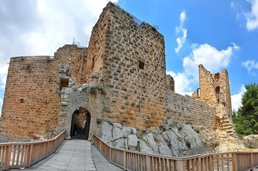 A historic stone castle with a central tower, a paved entrance pathway, and a surrounding stone wall. 4
