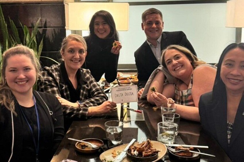 Un gruppo di persone sta cenando in un ristorante, a un tavolo con l'etichetta 'DELTA DELTA'. 2