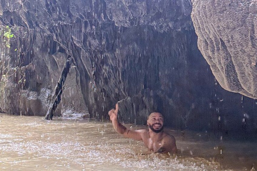 A person in a natural setting with a cave-like rock formation in the background. 3