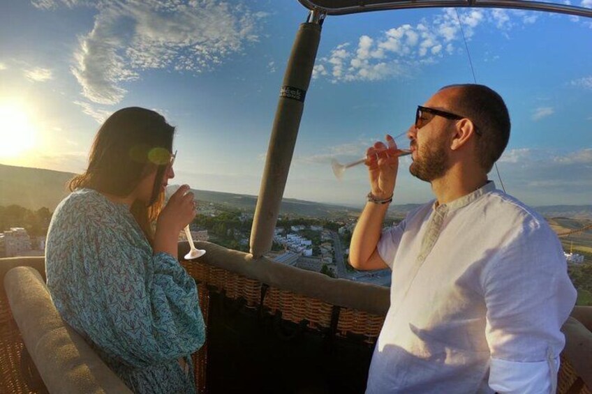 Dos personas sentadas en un balcón con vista a un paisaje urbano al atardecer. 3