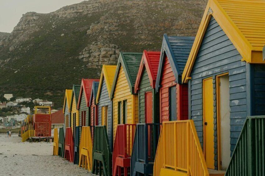 Färgglada strandhytter på rad med ett bergigt landskap i bakgrunden. 2