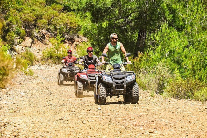 Tres personas montando vehículos todo terreno sobre un sendero de tierra rodeado de vegetación. 2