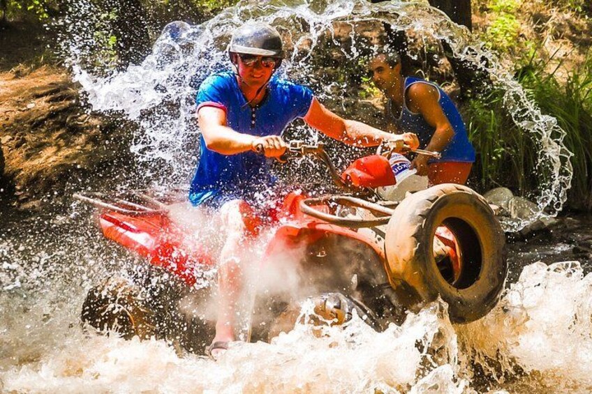 Dos personas con camisetas azules conducen un cuatrimoto rojo por el agua. 1