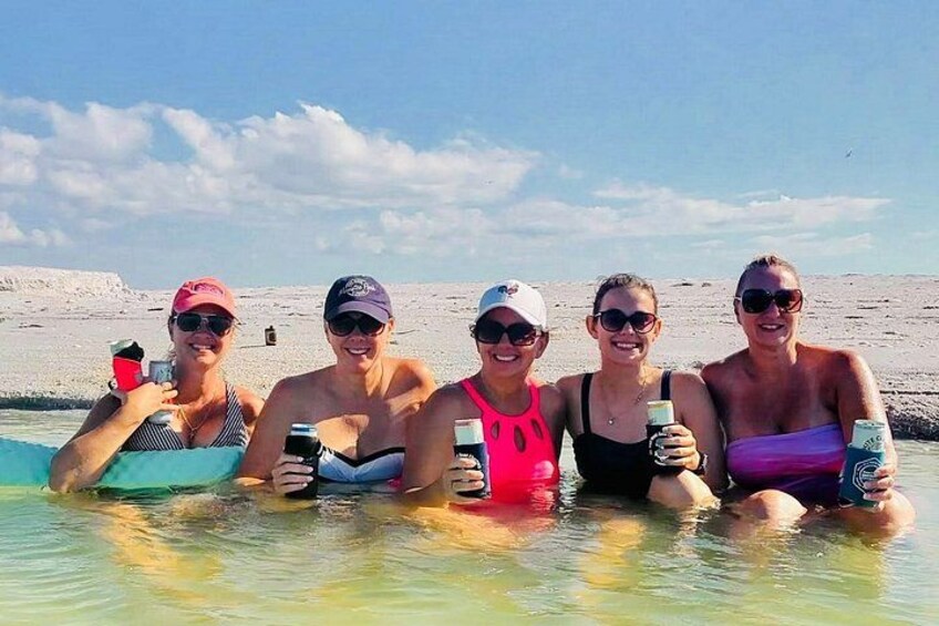 Un grupo de personas en una masa de agua poco profunda, posiblemente una playa, con cielo despejado y tierra en la distancia. 4