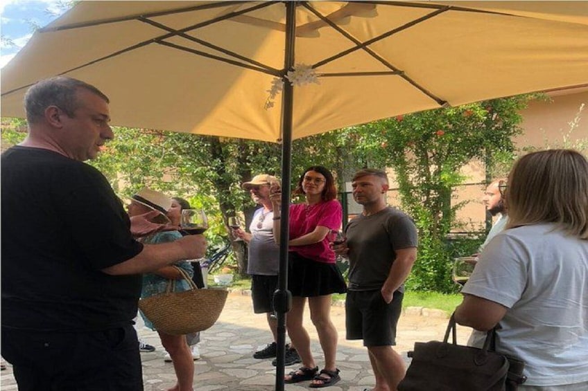 People standing under a tent, some holding drinks, with greenery in the background. 2
