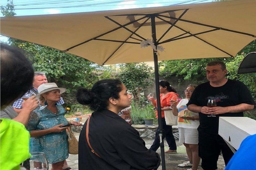 People standing under a canopy, some holding drinks, in an outdoor setting with greenery in the background. 3