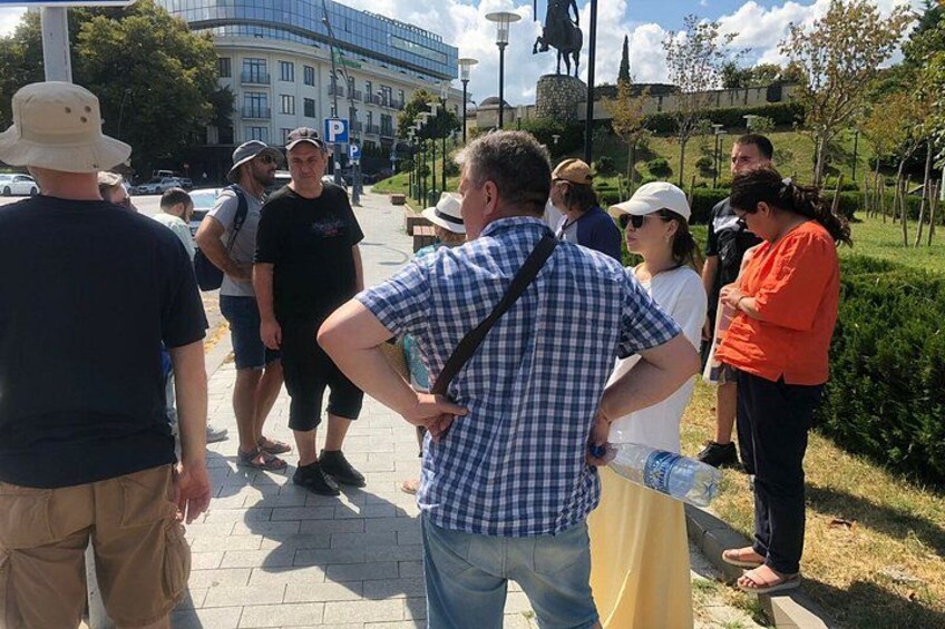 A group of people standing on a paved path in a park with a statue and a building in the background. 5