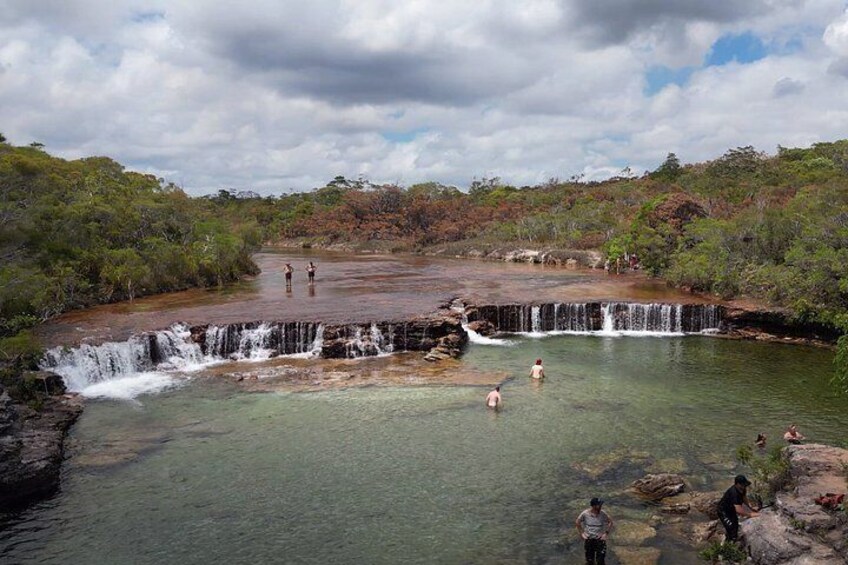 A waterfall, clear water, and people swimming. 3