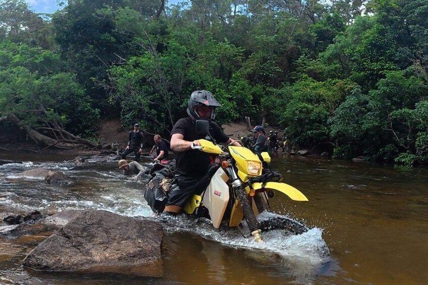 A person riding a yellow motorcycle over a rocky riverbed. 1