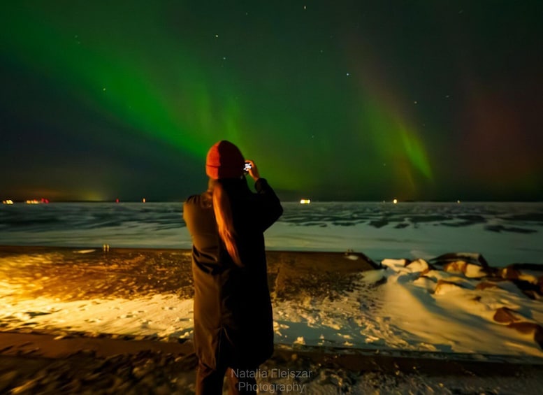 A person taking a photo of the aurora borealis over a snowy landscape. 1