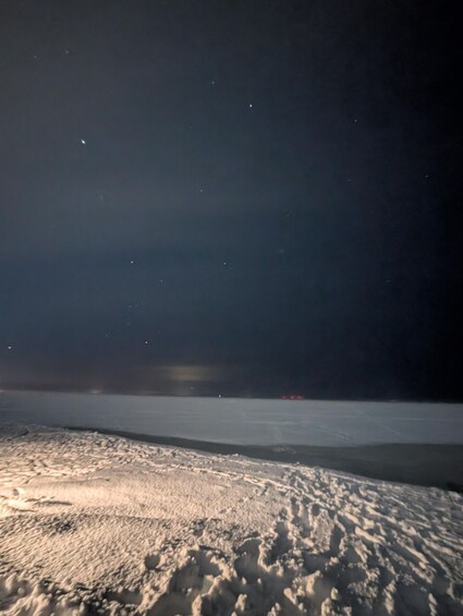 A snowy landscape at night with a clear sky and distant lights. 2