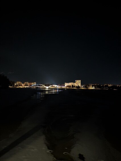 A nighttime cityscape with a river, a bridge, and illuminated buildings. 3