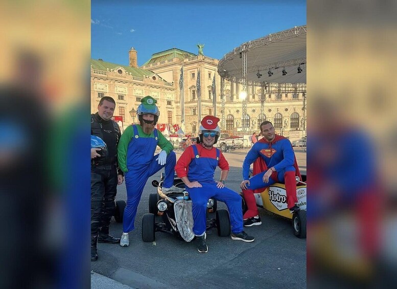 Quatre personnes déguisées : l’une porte un costume vert et bleu, une autre un costume rouge et bleu, et deux sont vêtues de costumes de Superman. Ils sont assis sur une charrette, avec un bâtiment en arrière-plan. 4