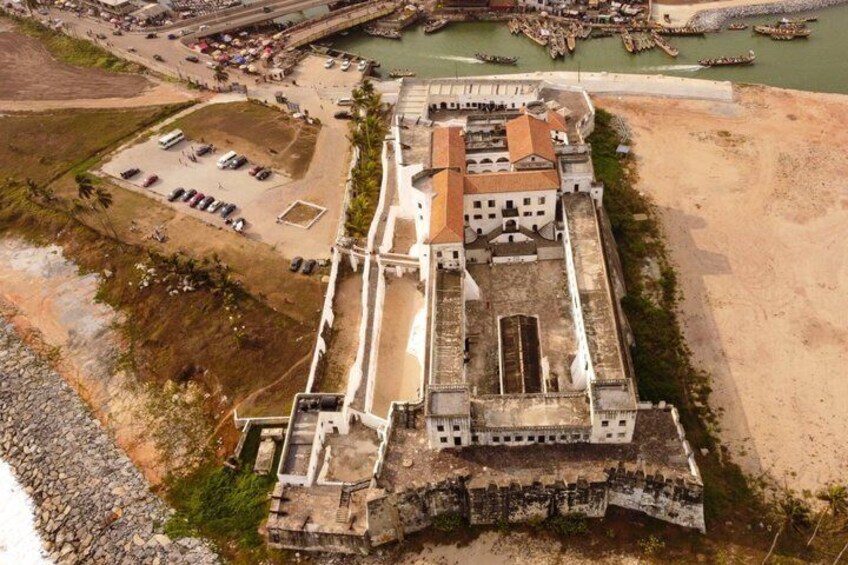 Vista aérea de una fortaleza histórica con un edificio central grande, un foso circundante y una zona de playa arenosa. 1