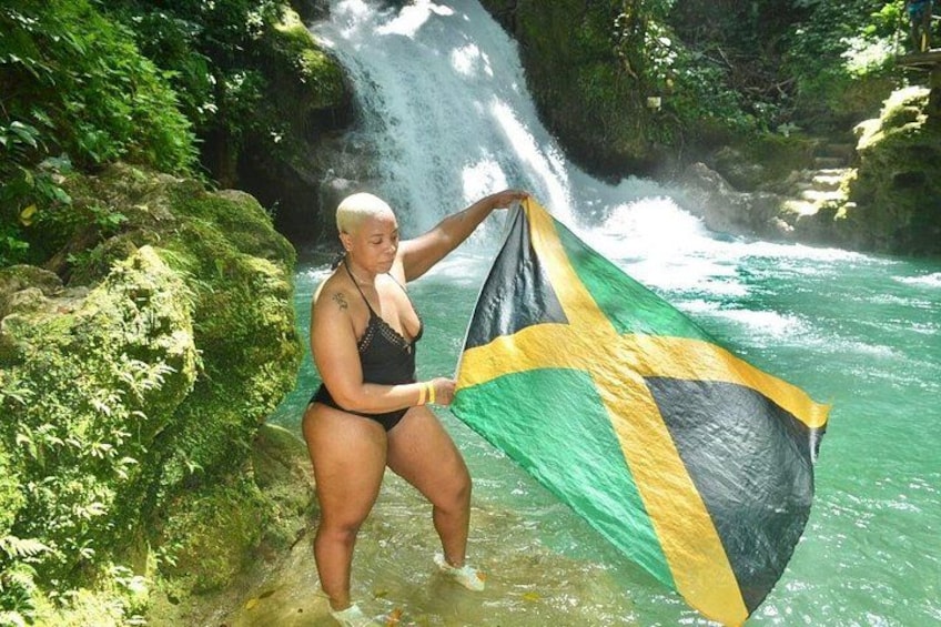 A person holding a flag by a waterfall in a forested area. 1