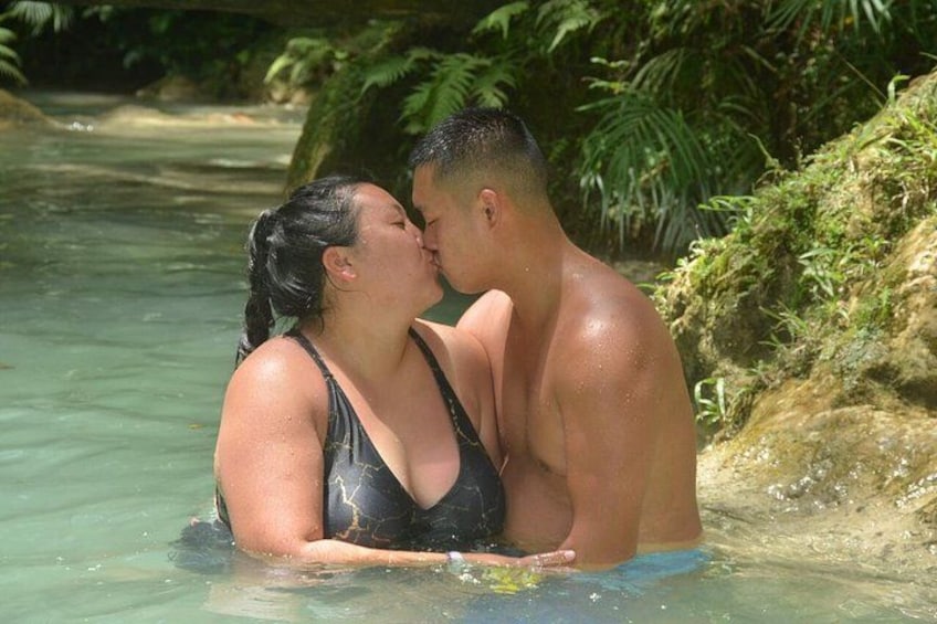 A couple in a tropical setting with clear water, surrounded by greenery. 3