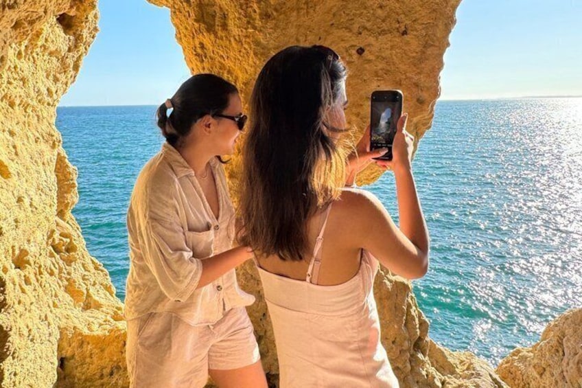 Dos personas fotografiando la entrada de una cueva costera, con el mar al fondo. 5