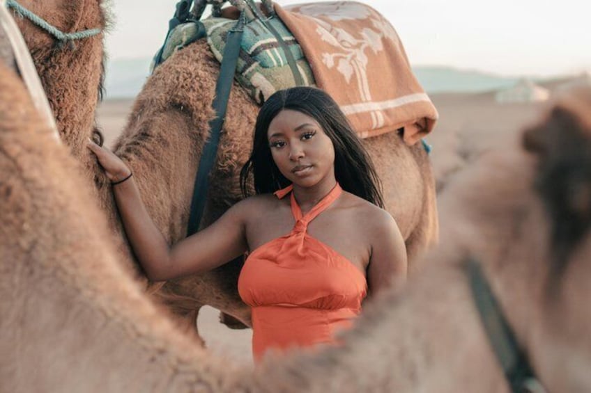 A person in an orange top sitting on a camel in a desert. 1
