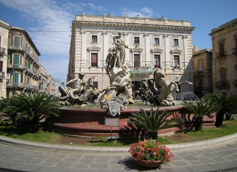 A classical fountain with sculptures in front of a building labeled "BANCO DI SICILIA". 5