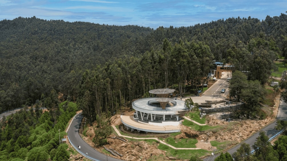 A circular building surrounded by a forested area with a road curving around it. 1