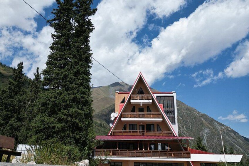 Eine Berglodge mit rotem Dach, Holzbalkonen und einer Aussicht auf Berge und Bäume. 4