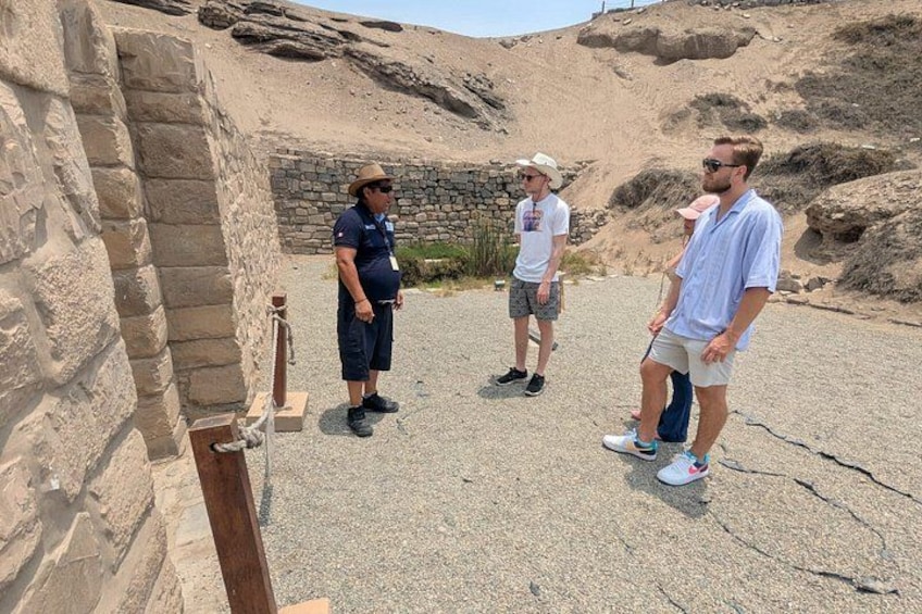 Un groupe de personnes se tient près d’une ancienne structure en pierre, dotée d’un mur de pierre et d’un poteau en bois. 2